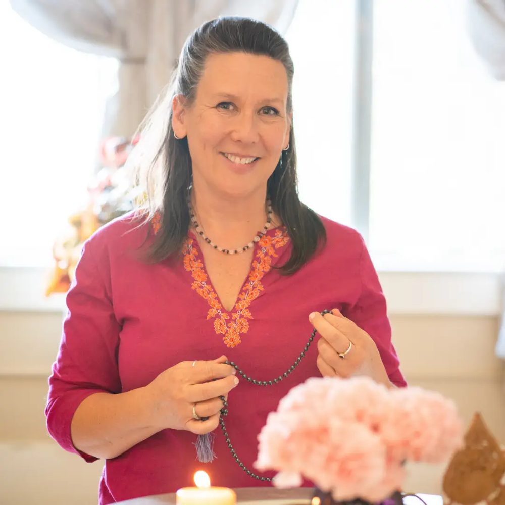 Aileen holding mala beads by a sunlit window